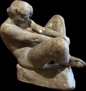 Joyous by Ben Solowey. Painted plaster to look like stone. Shows a seated female nude whose hands are slightly lifting one leg.